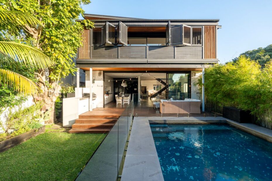 Modern two-story home with an open-plan living area opening to a pool deck and glass railing.