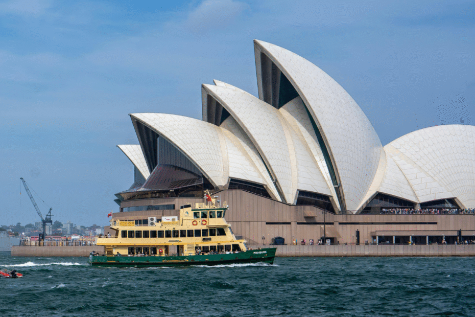 sydney opera house with its distinctive white sails on the harbor, a yellow ferry passing in the foreground under a blue sky