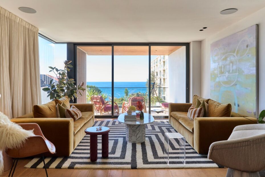 Living room with two tan sofas facing a glass wall that opens to a balcony with an ocean view.
